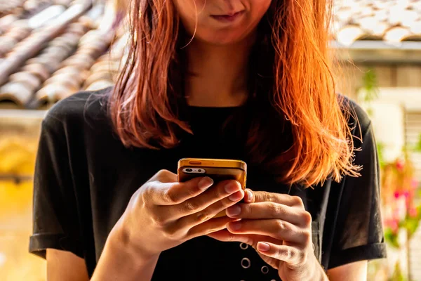 A close-up shot of an unrecognizable young Caucasian redhead woman looking down at her smartphone with a dissatisfied facial expression with an old French building in the background