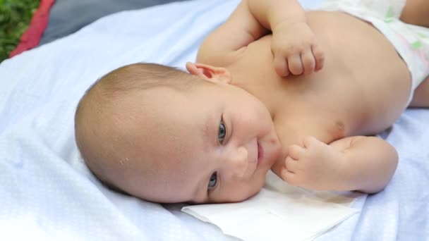 Cunningly smiling baby on a white sheet in a summer park. Handheld shot — Stock Video