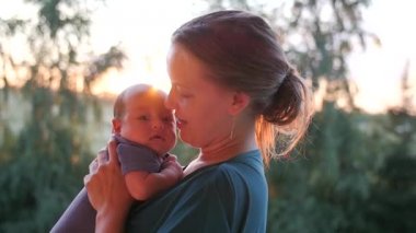 Mutlu genç kadın küçük bebeği akşam Park yükselterek. El atış