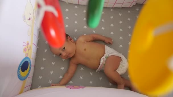 Neugeborenes in einer Windel. Blick von oben durch ein buntes mobiles Spielzeug — Stockvideo