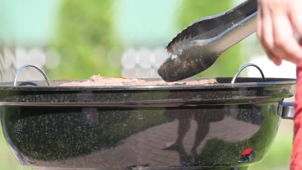 Barbbequing and turning meat upside-down with tongs. Handheld shot — Stock Video