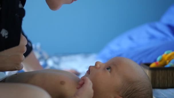 Gelukkig moeder haar baby in een blauwe bed liggen zoenen. Handheld schot — Stockvideo