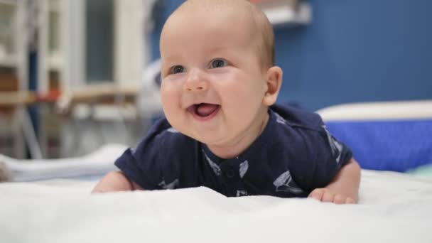 Menino feliz deitado de barriga em uma cama e rindo. Tiro portátil — Vídeo de Stock