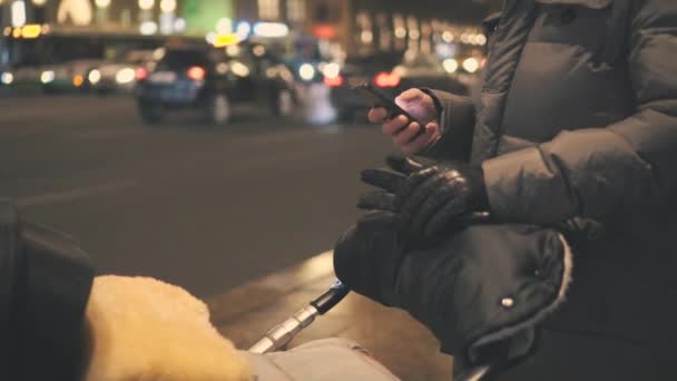 Ο άνθρωπος με το μωρό μεταφορά σε έναν δρόμο χρησιμοποιεί smartphone. Θολή φανάρια μαρμελάδα — Αρχείο Βίντεο