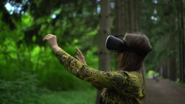 Женщина в защитных очках пытается прикоснуться к объектам в виртуальной реальности. Зеленый парк в качестве фона — стоковое видео