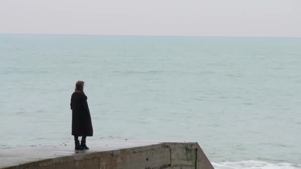 Lonely woman on concrete breakwater looks at the distance. Cold sea and overcast sky. Handheld shot — Stock Video