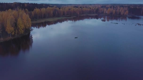 Маленькая моторная лодка плавает на волнистой голубой воде озера среди осенних лесов. Воздушный удар — стоковое видео