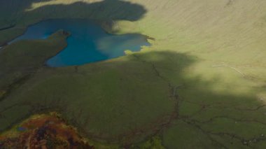 Caldeirao yanardağının yeşil yamaçlarında güneş ışığı ve gölgeler. Corvo Havalimanı, Azores