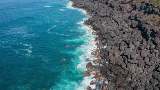 Ar de costa rochosa. Ondas oceânicas azuis quebram em pedras pretas em espuma branca — Vídeo de Stock