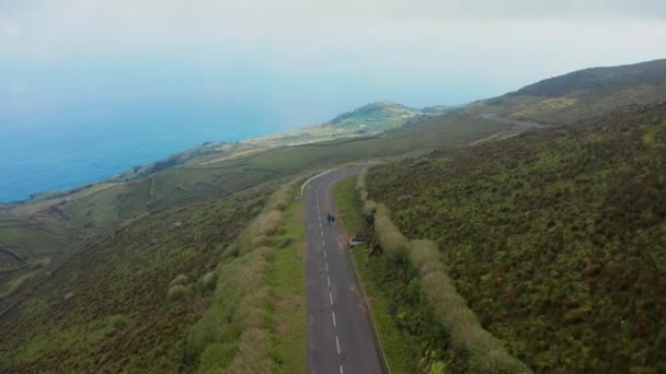 Dos personas caminan por el camino que conduce a la cima de la montaña en la isla en el océano. Foto aérea de Corvo, Azores — Vídeos de Stock
