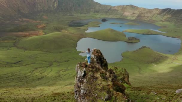 Meisje met wijd open armen op een rots boven rooster en mooie groene caldera van inactieve vulkaan. Luchtfoto van Corvo, Azoren — Stockvideo