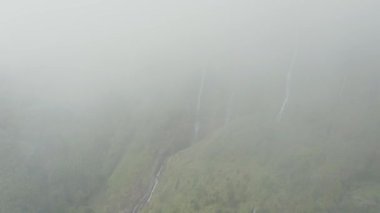 Su akıntıları ile dik yamaç. Ferreiro şelalesi tepedeki bir bulutta kaybolur.