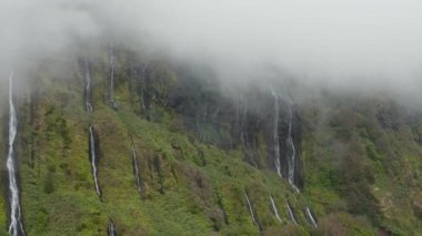 Ferreiro sarp kayalıklarda dalgalanır. Bulutların arasından su düşüyor. Flores Adası, Azores Havalimanı