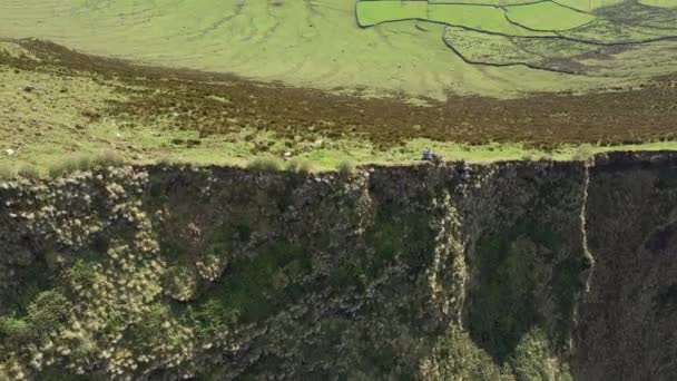 Zwei Personen am Rande steiler Klippen blicken auf die riesige Caldera. Antenne des Vulkans Caldeirao, Corvo, Azoren — Stockvideo