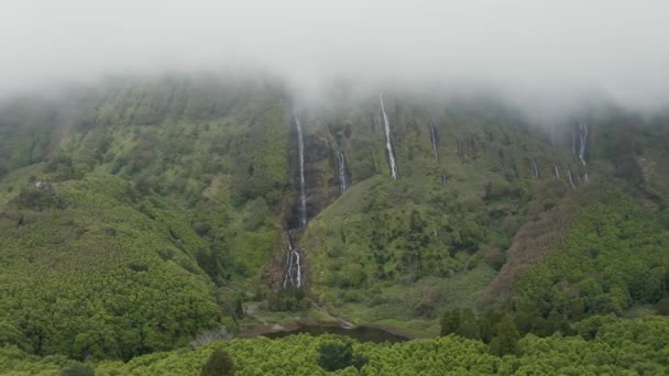 Low cloud covers mountain top. Waterfall streams on green steep slope. Aerial of Ferreiro, Flores, Azores — ストック動画