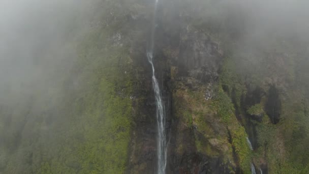 Levegő a felhőből a magas vízesésnél. Meredek lejtők, sziklák és zöld növények. Ferreiro, Flores, Azori-szigetek — Stock videók