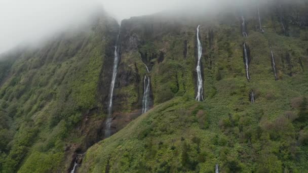 Water falls from cliff. Ferreiro waterfall and mountain disappear in cloud. Aerial of Flores, Azores — ストック動画