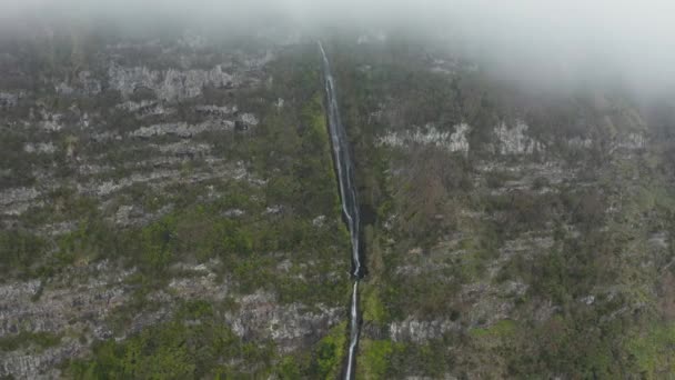 Flujos de cascada desde el estrecho desfiladero en el acantilado rocoso. Nube cubre la cima de la montaña. Aérea de Flores, Azores — Vídeo de stock