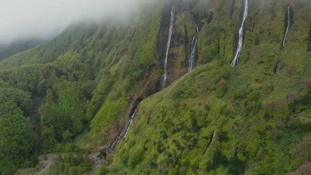 Fliegen in einer Wolke auf dem Gipfel des Berges mit Wasserfall an seinem grünen steilen Hang. Antenne von ferreiro waterfal, flores, azores — Stockvideo