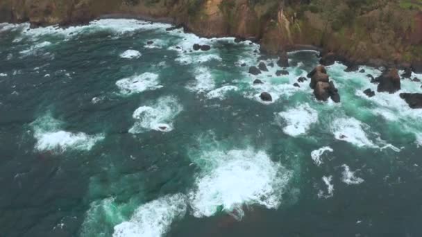 Bovenaanzicht van oceaangolven die kustrotsen raken en wit schuim maken. Luchtfoto — Stockvideo