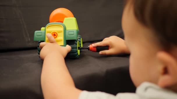 Маленька дитина грає з пластиковою машиною. Ремонт іграшкового бетономішалки з викруткою — стокове відео