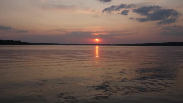 Cielo del atardecer sobre las aguas ondulantes de un lago. Sol rojo en las nubes sobre el horizonte — Vídeos de Stock