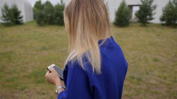 Achteraanzicht van een vrouw met smartphone chatten tijdens het lopen langs een gazon — Stockvideo