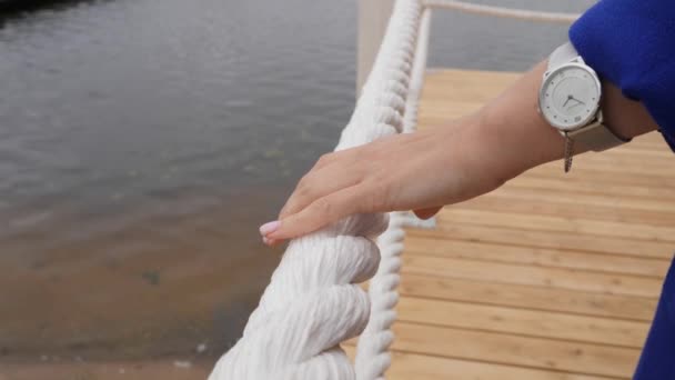 Femme touche avec ses doigts une corde épaisse utilisée comme balustrade sur une jetée de lac. Gros plan — Video