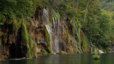 Plitvice Gölü 'ne yeşil bitkilerle kaplanmış kayalık kıyılardan akan şelale akıntıları