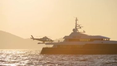 Tahtasında helikopter olan modern bir yat. Sakin denizin üzerinde gün batımı