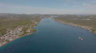 Tepe kıyılarının arasında, uzun deniz koyunun üzerinde uçuyor. Uzakta beyaz köprü