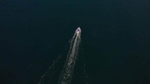 Mar azul profundo e pequeno barco a motor. Pista branca na superfície da água. Tiro aéreo — Vídeo de Stock