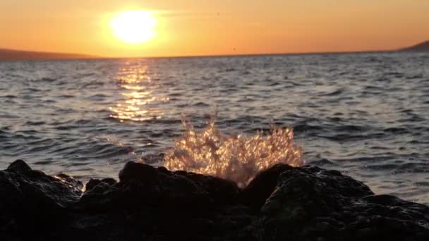 Rochas pretas e salpicos de onda piscando na luz do pôr do sol. Marítima — Vídeo de Stock