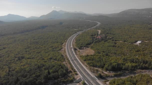 Flygfoto av modern asfalterad motorväg som passerar genom skog till berg — Stockvideo