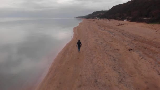 Man runs on winter beach, picks up flat stone and throws it to sea. Stone skipping art — Stock Video