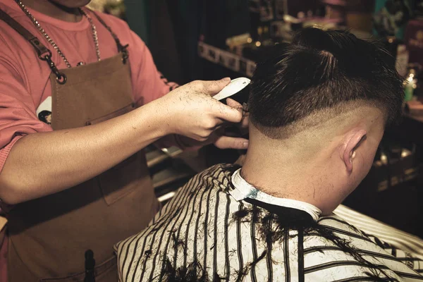 Young guy hairdresser cuts hair with trimmer to a man in a beauty salon.