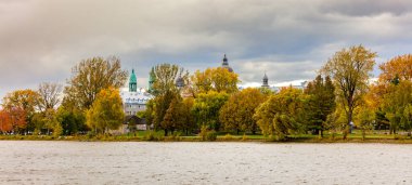 Arka planda antik yapı kubbeleri olan nehir kıyısındaki sonbahar parkının manzarası