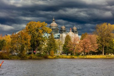 Arka planda antik yapı kubbeleri olan nehir kıyısındaki sonbahar parkının manzarası