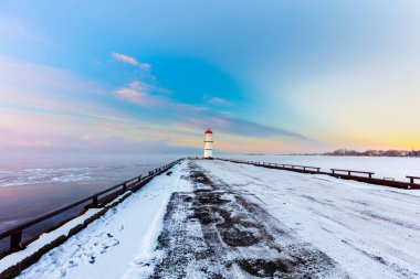 Donmuş deniz kıyısındaki güzel deniz fenerinin kış günbatımında çekilen manzarası.