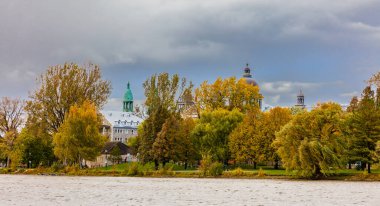 Arka planda antik yapı kubbeleri olan nehir kıyısındaki sonbahar parkının manzarası