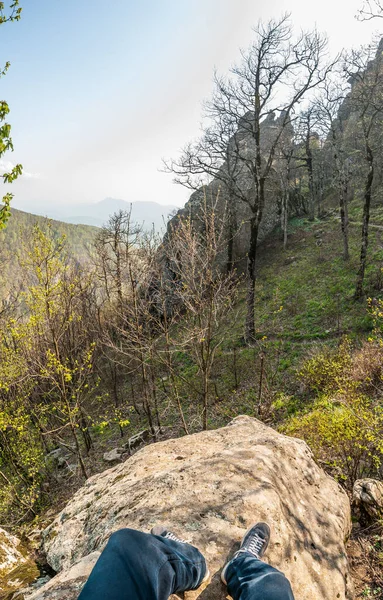 Dağdaki bir kayadan birinci şahıs manzarası, dağdaki bahar ormanı, çerçevedeki bacaklar..
