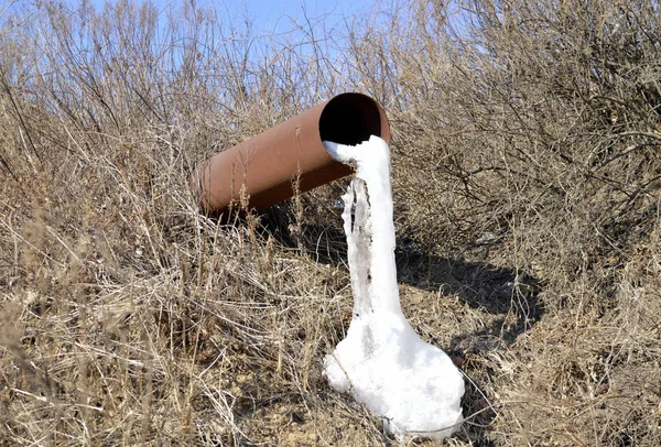 Old rusty pipe with frozen dirty water in a poor area