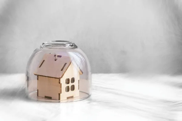 El concepto de cuarentena, quédate en casa. Una pequeña casa de madera está protegida por una cúpula de vidrio transparente. Fondo gris borroso, enfoque selectivo — Foto de Stock