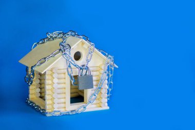 The concept of isolation. Stay at home. Quarantine during an epidemic. House arrest. Wooden house on a metal chain with a lock on a blue isolated background clipart
