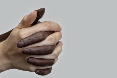Gri izole bir arka planda el sıkışarak bir yumruğa toplanmış siyah-beyaz insan elleri. İnsanlar arasında ırkçılık, dostluk ve saygıyla mücadele kavramı. Seçici odaklanma, yakın plan..