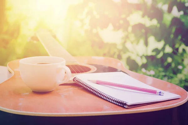 Las guitarras acústicas con un cuaderno y una taza de café en la mesa, la música relajarse en el jardín — Foto de Stock