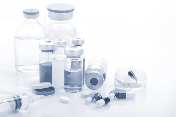Injektionsflaskor av glas medicin med spruta och tabletter kapsel på vitt bord medicinsk koncept — Stockfoto