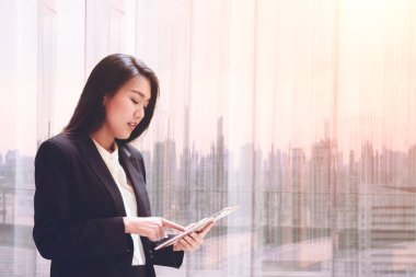 Tablet cam kenarında relax için kullanma zarif genç iş kadını ekran ve iş bölgesine bakarak arka plan bulanık