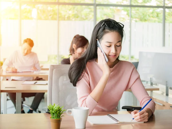 Joven mujer de negocios hablando en el teléfono inteligente y utilizando la escritura en el concepto de cuaderno para la orden de recepción o apoyo al consumidor —  Fotos de Stock