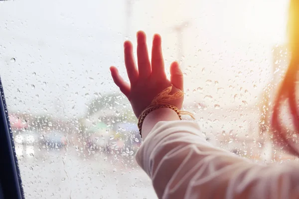 在下雨的日子里, 小女孩的手从窗户往外看, 车窗上有闪光灯和雨滴落在车门玻璃上 — 图库照片